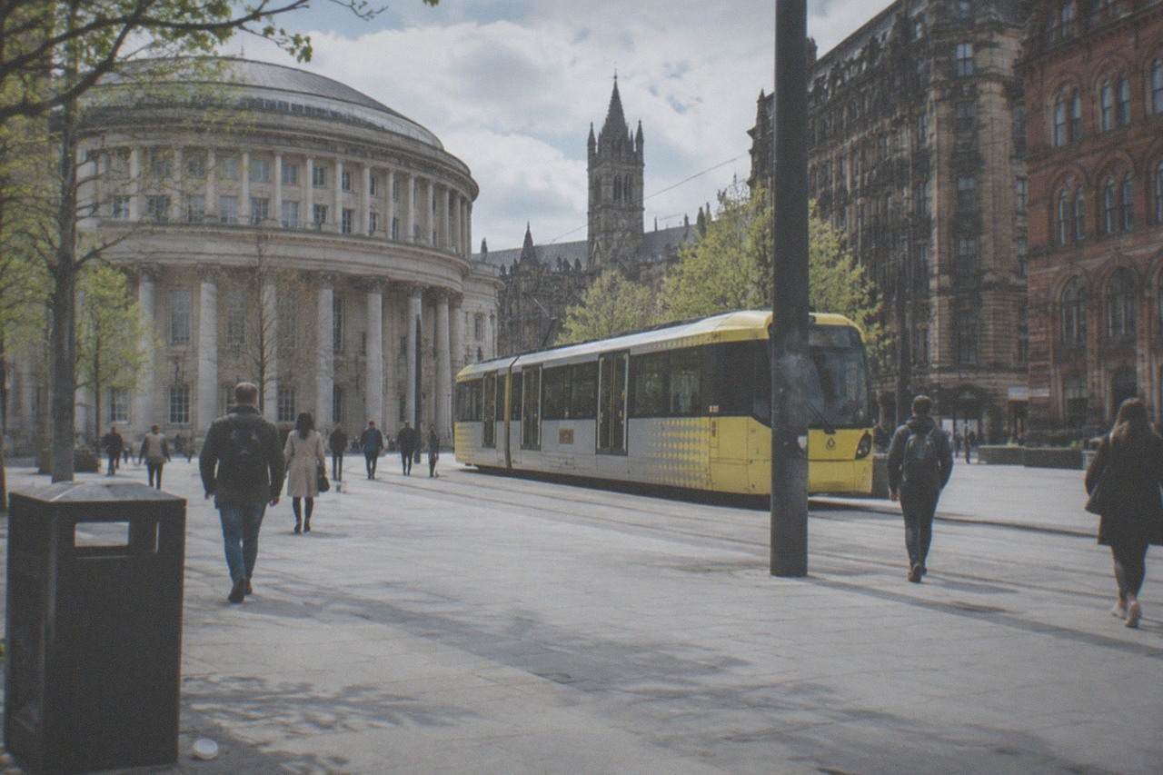 Visitors walking through a busy Manchester city centre square with historic brick buildings and a tram passing by