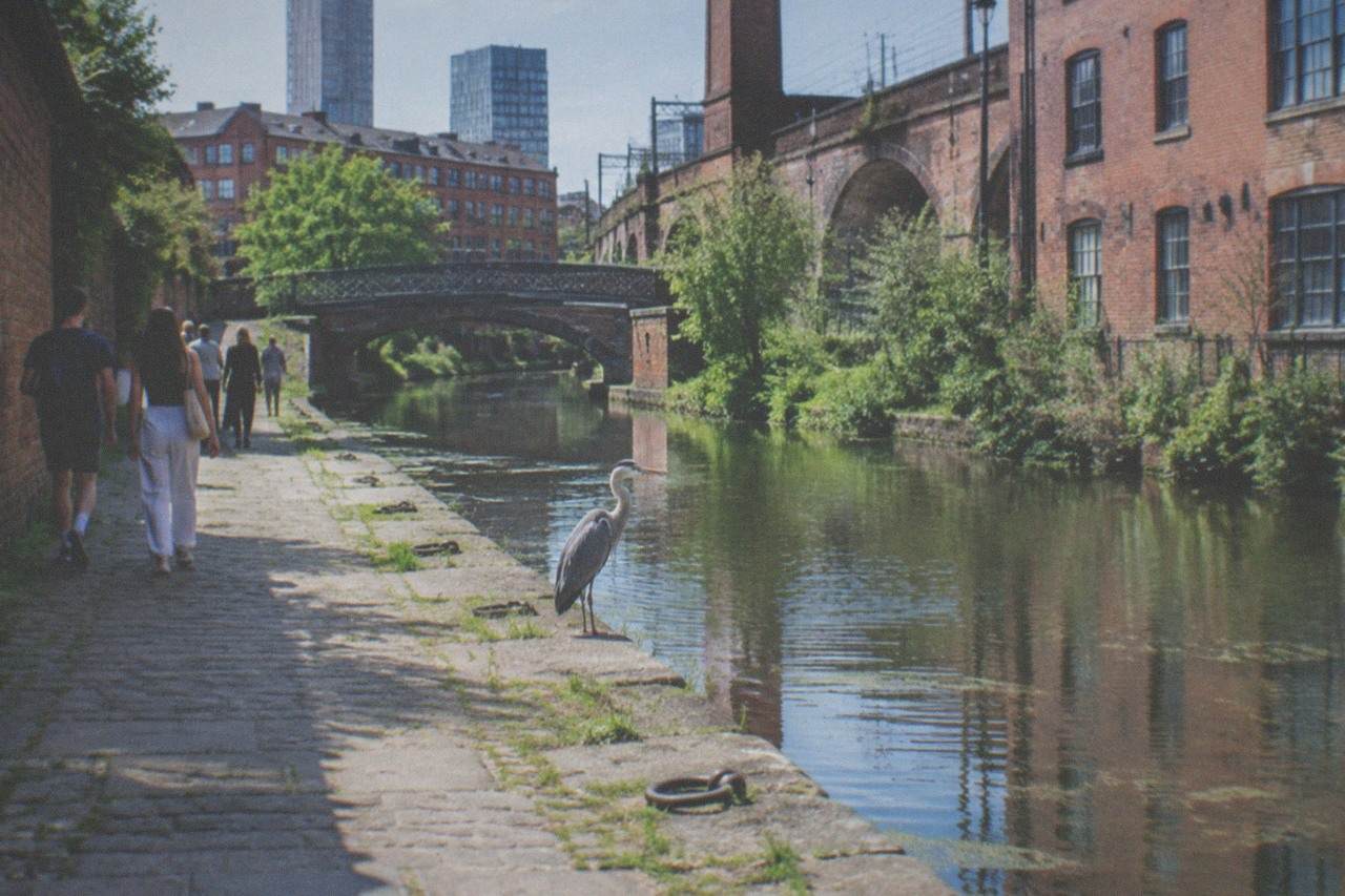 Visitors walking past the brick warehouses and canal basins of Castlefield in central Manchester on a bright afternoon