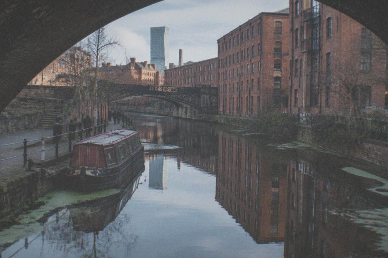 Manchester's Castlefield canal basin with red brick warehouses and a railway viaduct reflected in the water
