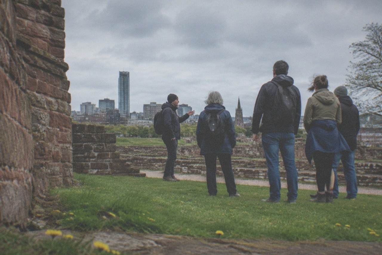 A guide addressing a small group of visitors at a meeting point in central Manchester before a free walking tour