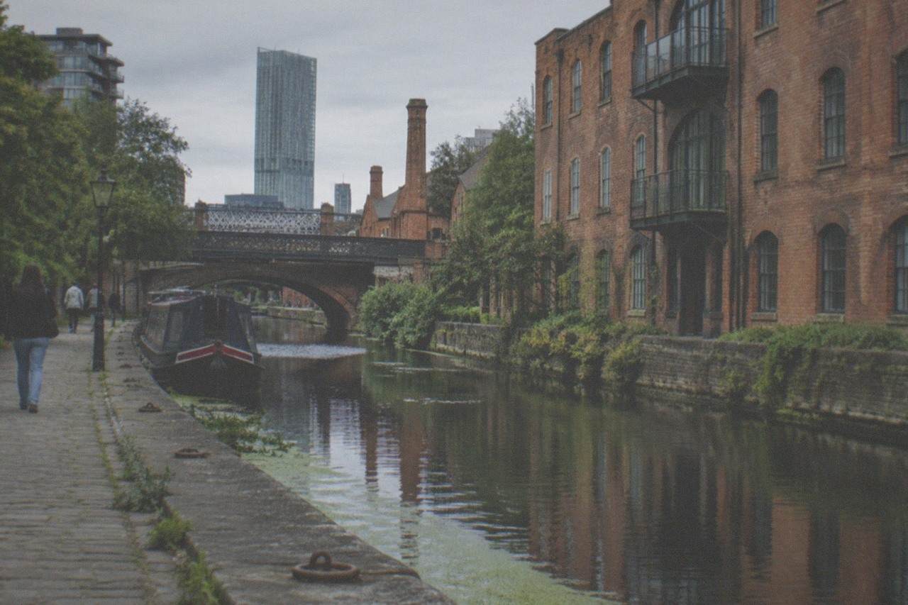 Visitors walking beside the restored brick warehouse walls and canal basins of Castlefield in central Manchester